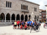 Eine Radlergruppe posiert vor einem Gebäude mit einer männlichen Statue in Udine