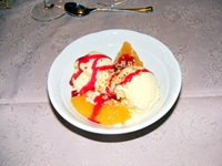 Ein Nachtischteller mit zwei Kugeln Eis, etwas Obst, einer roten Soße und Nüssen als Garnierung