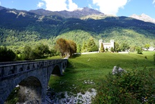 Eine steinerne Brücke im Bergell führt auf den Palazzo Castelmur zu, hinter dem sich ein traumhaftes Bergpanorama erhebt.