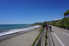 Eine Radfahrerin in Ligurien macht am Rand eines Radwegs, der direkt an der Küste entlangführt, Pause.