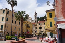 Cafés und Restaurants in der idyllischen Fußgängerzone von Laigueglia werden von den Doppeltürmen der Kirche San Matteo und mächtigen Palmen überragt.