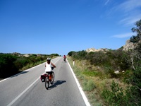 Zwei Radlerinnen fahren auf einer asphaltierten Straße an den teilweise bizarren Felsformationen der Gallura vorbei.