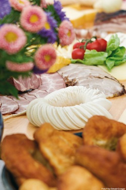 Eine schmackhafte Brotzeit mit Rettich, verschiedenen Schinkenspezialitäten und Gemüse auf einem mit Blumen geschmückten Tisch.