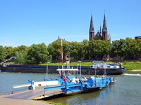 Eine weiß-blaue Fähre liegt am Flussufer der Maas und wartet auf die letzten Passagiere.