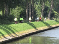 Eine Radlergruppe fährt an einem Wasserlauf entlang.