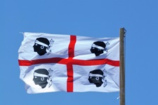 Die sardische Flagge mit dem roten Kreuz und den vier abgeschlagenen Mohrenköpfen weht im Wind.