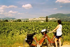 Eine Frau steht neben zwei abgestellten Rädern und blickt über ein Feld zu einer Stadt