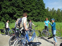 Eine Radlergruppe steigt nach einer Pause wieder auf ihre Räder und lauscht dabei ihrer Reiseleiterin.