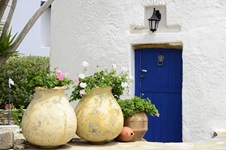 Drei Blumentöpfe mit rosa und weißen Blumen vor einem Haus mit einer blauen Tür