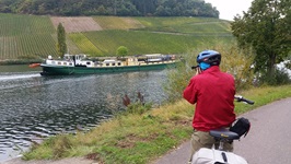 Ein Fahrradfahrer steht am Ufer und blickt auf die La Belle Fleur, die auf dem Fluss fährt