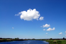 Strahlend blauer Himmel mit einigen weißen Wattewölkchen über einem Flusslauf.
