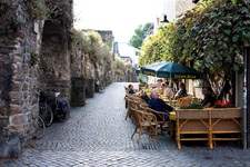 Touristen und Einheimische sitzen unter grünen Sonnenschirmen in einem Straßencafé in der Altstadt von Maastricht.