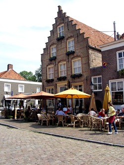 Menschen sitzen vor einem markanten Treppengiebelhaus am Markt von Heusden in einem Straßencafé.