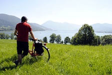 Ein Radfahrer steht mit seinem Rad auf einer saftig grünen Wiese und blickt zum Chiemsee und den dahinterliegenden Alpen