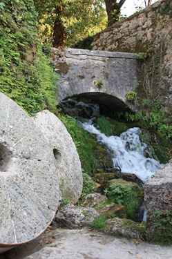 Zwei Mühlsteine liegen unterhalb einer romantischen Steinbrücke, die über einen sprudelnden Wildbach in Dalmatien hinwegführt.