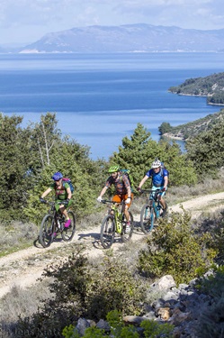 Drei Mountainbiker biken in einem Nationalpark Dalmatiens vor der traumhaften Kulisse der tiefblauen Adria.