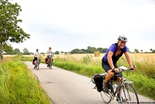 Drei Radfahrer radeln auf einem asphaltierten Weg an einem Feld in Dänemark vorbei