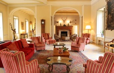 Blick in einen Aufenthaltsraum mit offenen Kamin und rot-beige gestreiften Ohrensesseln des Hotels Sina Villa Matilde