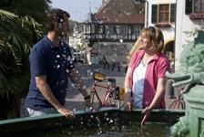 Zwei Radler haben ihre Räder abgestellt und erfrischen sich am Andreasbrunnen in Deidesheim.