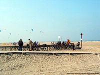 Blick auf einen Radler-Strand mit vielen abgestellten Rädern und einige Fahrradfahrern