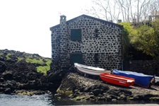 Bunte Ruderboote liegen vor einem alte Steinhäuschen an Land.