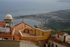 Bunte Häuser und ein Kirchturm überragen eine sizilianische Meeresbucht.