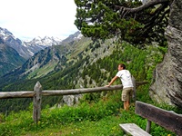 Ein Wanderer genießt den herrlichen Ausblick auf grüne Wiesen und schneebedeckte Gipfel, der sich ihm beim Torre Belvedere oberhalb von Maloja bietet.