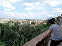 Ein Radfahrer steht in der Toskana an einer Steinmauer und schaut auf die vor ihm liegende Stadt.