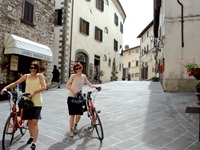 Zwei Radlerinnen schieben ihre Räder durch eine Fußgängerzone in der Toskana.