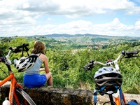 Eine Radlerin sitzt in der Toskana auf einer Steinmauer und genießt den schönen Ausblick.