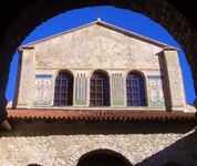 Die Euphrasius-Basilika in Porec mit ihrem Arkadenunterbau und kunstvollen Außenfresken, die Kerzen sowie verschiedene Apostel/Heilige zeigen.