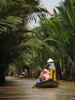 Touristen fahren mit einem typischen Boot, das von einem Vietnamesen geführt wird, durch das Mekong Delta