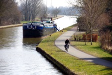 Radfahrer auf einem Radweg neben einem Fluss im Elsass auf dem ein Schiff angelegt ist