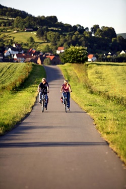 Zwei Radler fahren auf dem Weser-Radweg an reifenden Kornfeldern vorbei.