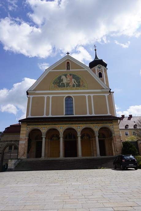 Die Erzabtei St. Martin zu Beuron mit ihrer markanten ockerfarbenen Fassade, dem Eingangsbereich mit Bögen und dem zentralen Mosaik mit weißenm Pferd und Reiter