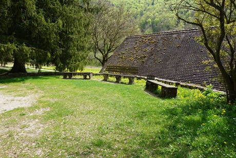 Idylllische Sitzgruppe im Grünen mit drei Bänken und einem Haus dahinter, von dem man nur das Dach sieht, direkt gegenüber der Mauruskapelle
