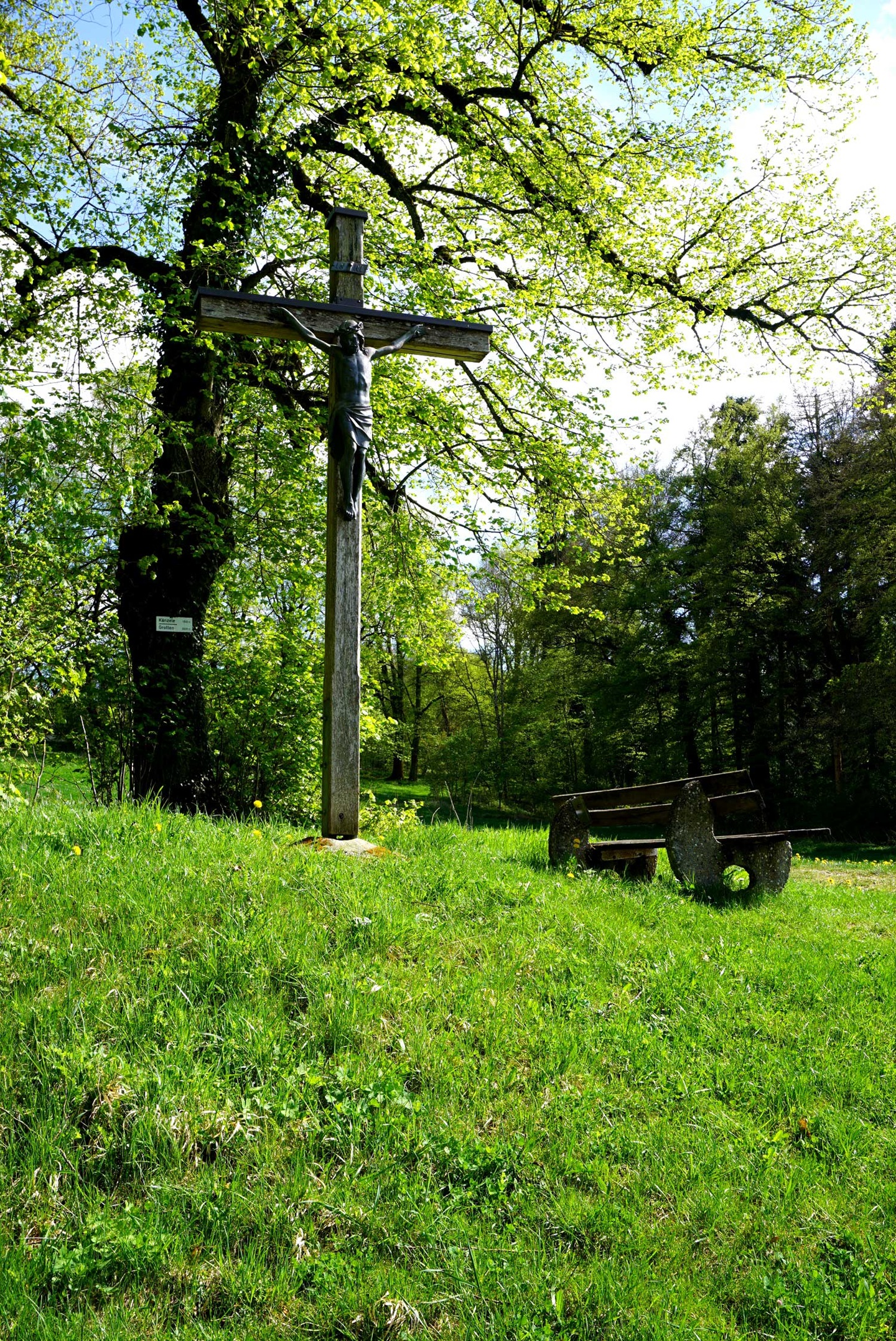 Das Holzkreiz mit Jesusfigur, inmitten eines grünen Waldes in Inzigkofen und einer Ruhebank davor - Naturpark Obere Donau