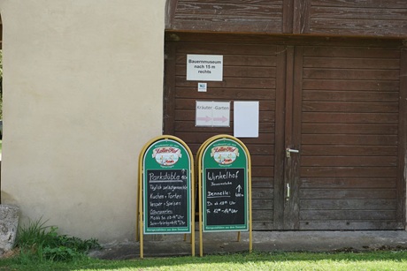 Aufsteller vor einer Holztür im ehemaligen Kloster Inzigkofen mit Informationen zu Öffnungszeiten von umliegendem Imbiss und Gasthaus