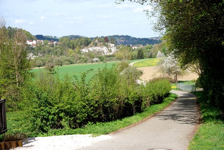 Schmaler asphaltierter Weg mit Blick in Richtung des Ortes Laiz, umgeben von üppigem Grün und Blick auf die weite Landschaft