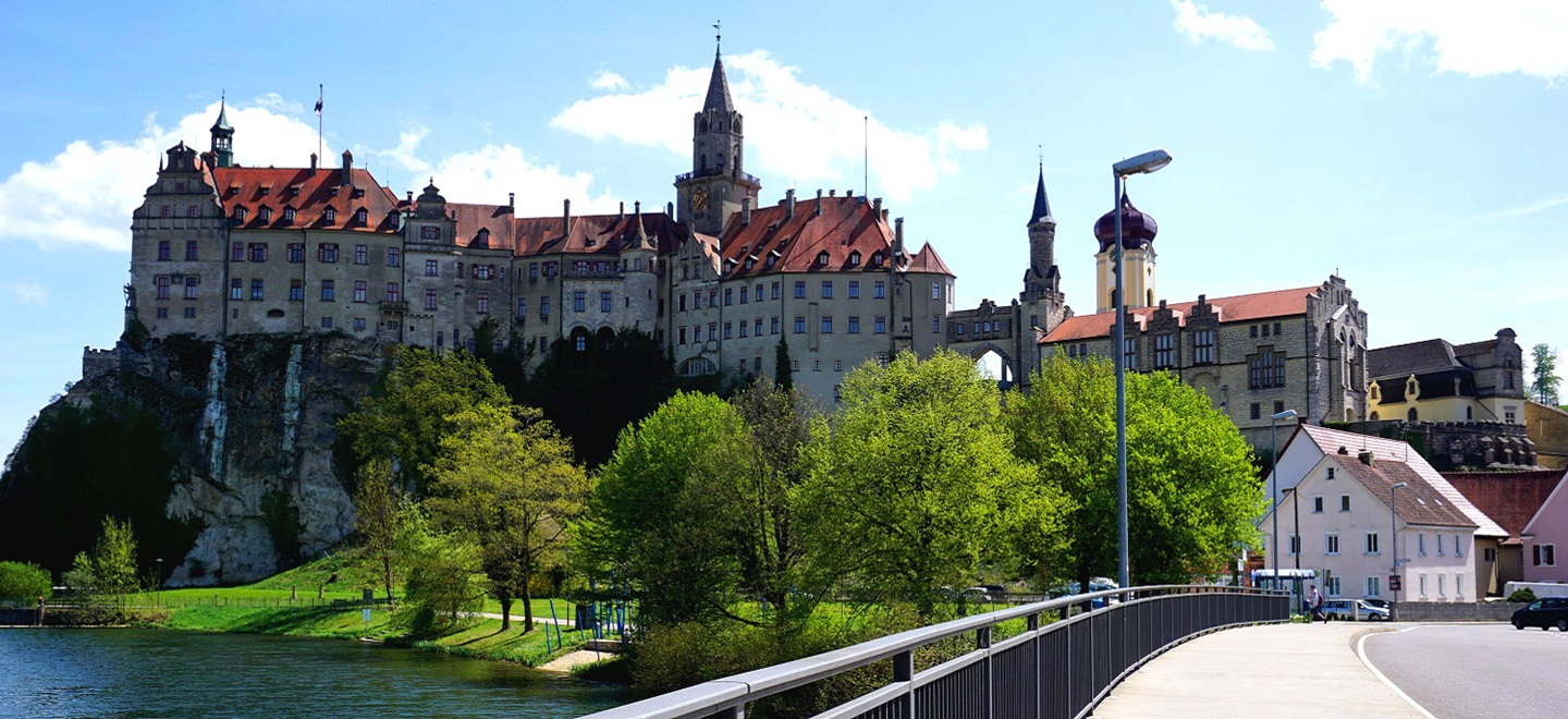 Das Schloss Sigmaringen mit seiner markanten Lage auf einem Felsen direkt am Ufer der Donau, umgeben von grünen Bäumen und einem modernen Brückenbau