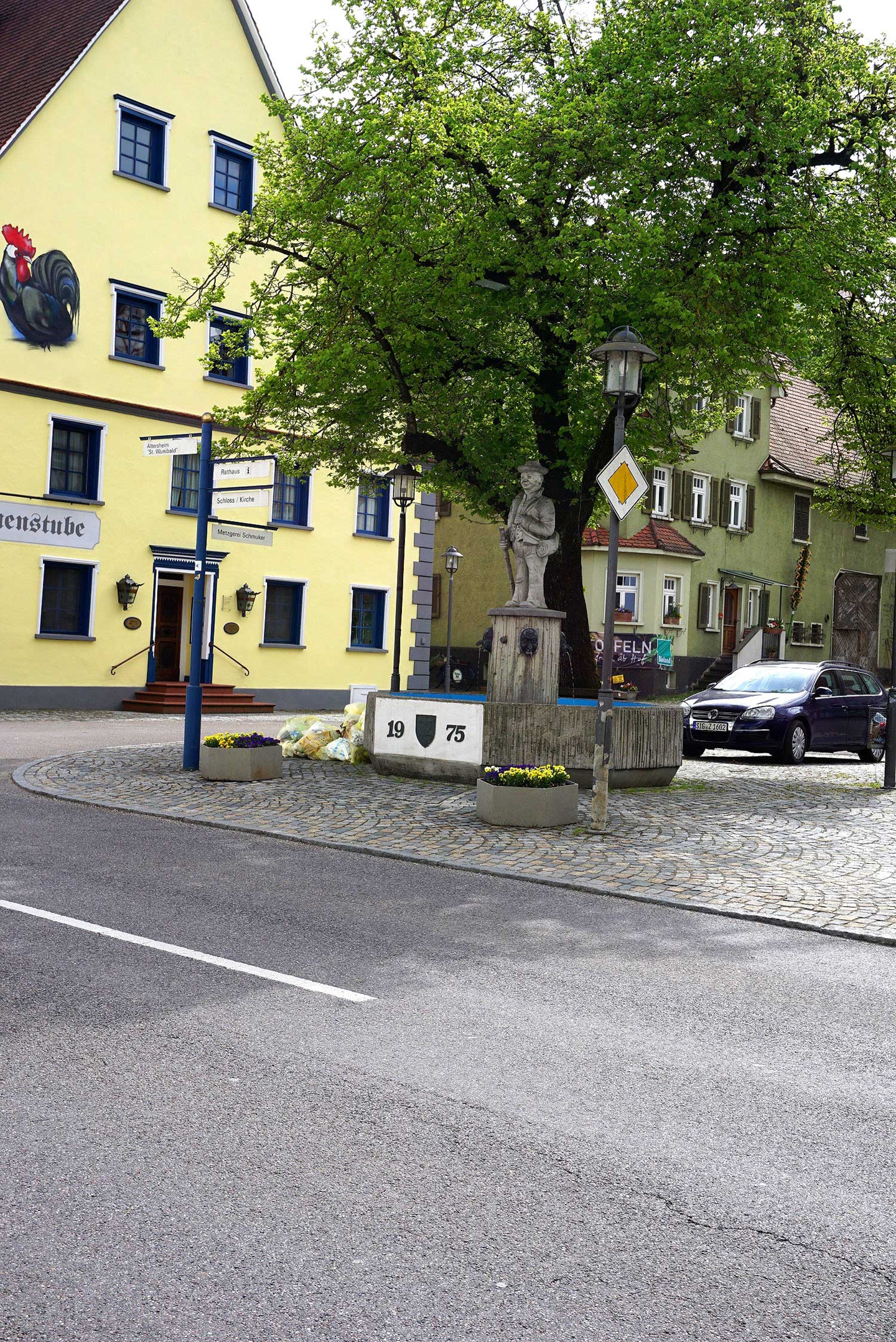 Steinerne Statue eines bäuerlichen Mannes, die auf einem Brunnensockel in Scheer steht.