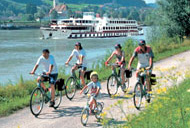 Radlerfamilie neben der Donau, auf der die MS Theodor Körner fährt