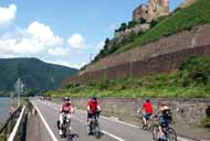 Radler auf dem Rhein-Radweg bei Rüdesheim, rechts oben eine Burgruine
