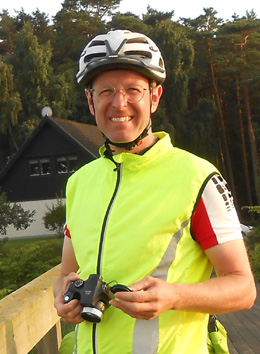 Guido Sackmann in einer leuchtend gelben High-Visibility-Weste und einem weißen Fahrradhelm, der eine Kamera in den Händen hält