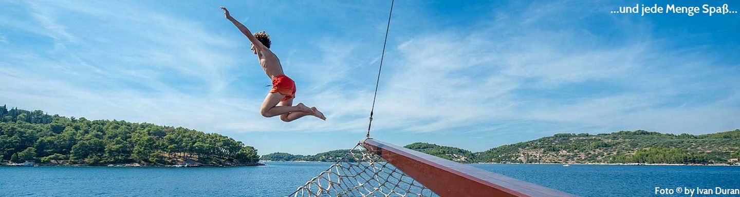 Ein Kind mit orangener Badehose springt vom Schiff in das Meer, Dalmatien