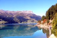 Blick über einen See, im Hintergrund die hoch aufragenden Berge, Südtirol