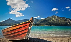 Ein hölzernes Ruderboot vor einer traumhaften Voralpenkulisse an einem See in Bayern.