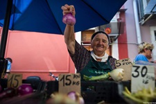 Eine ältere Frau präsentiert an ihrem Marktstand in Motovun eine rote Zwiebel und eine Fenchelknolle.
