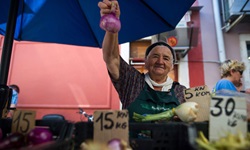 Eine ältere Frau präsentiert an ihrem Marktstand in Motovun eine rote Zwiebel und eine Fenchelknolle.
