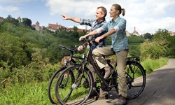 Zwei Radfahrer auf einem geteerten Weg halten am Flussufer bei Rothenburg - ein Mann zeigt mit seinem Finger auf etwas